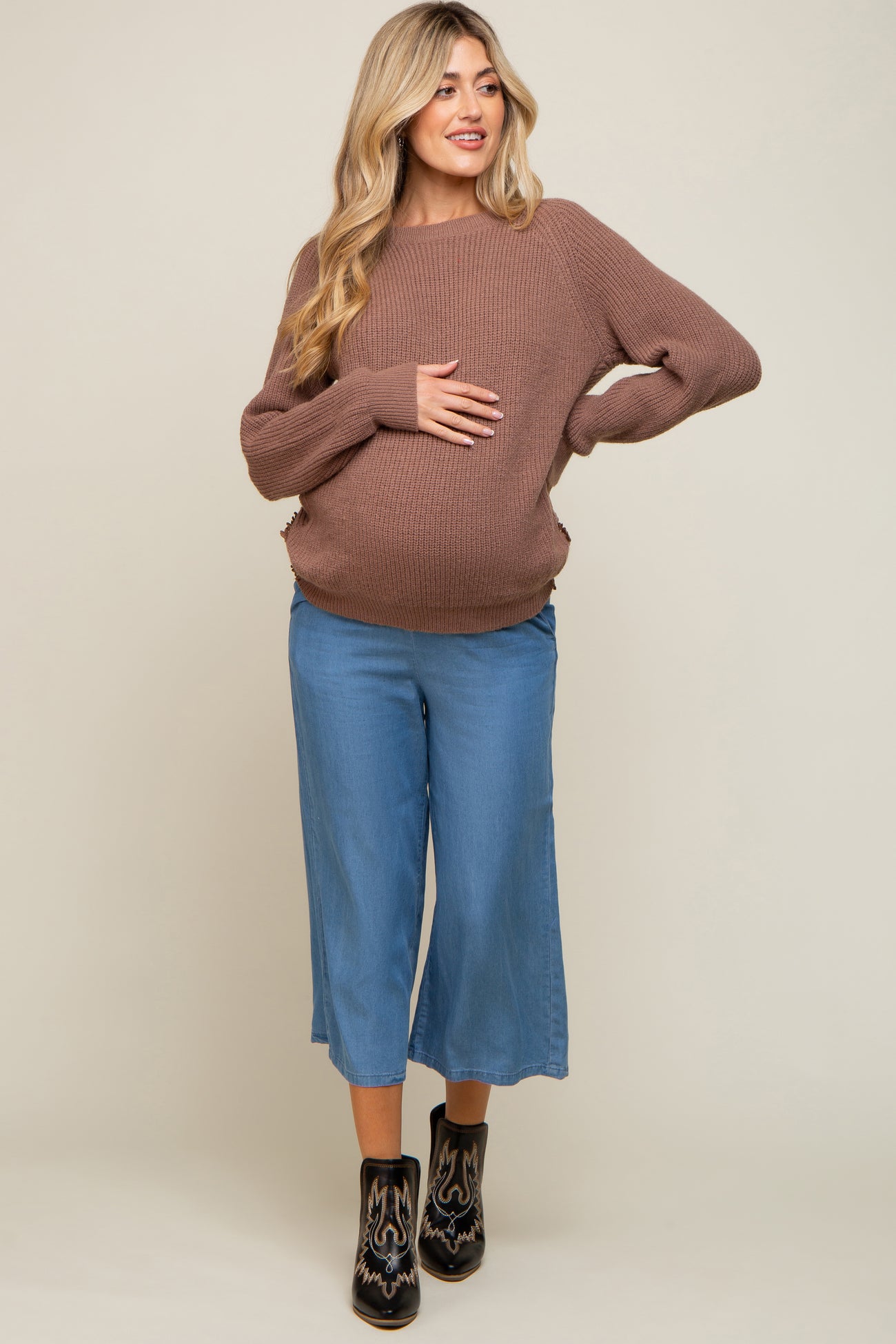 pregnant woman wearing a brown knit maternity sweater and blue wide leg pants with black boots