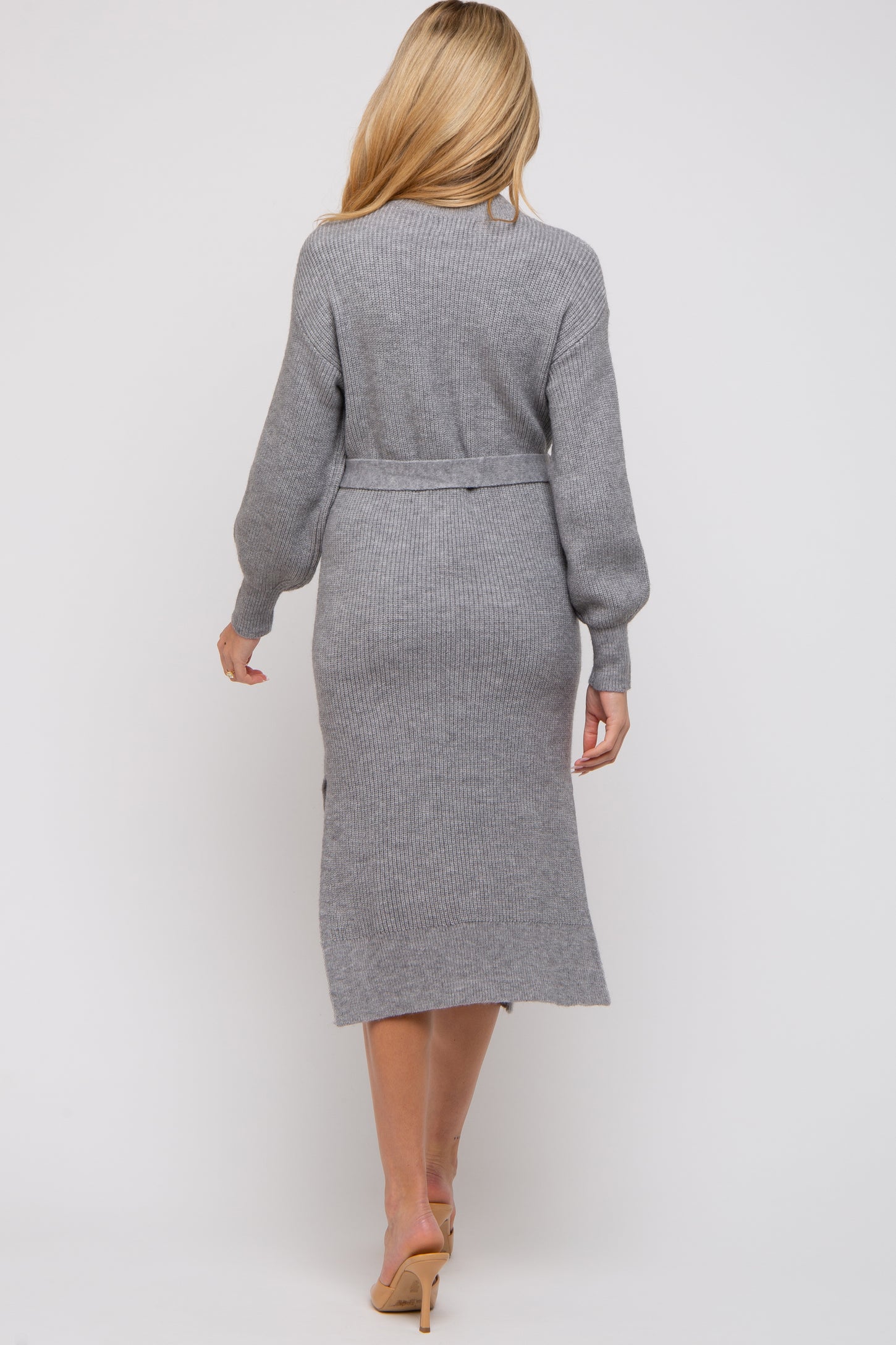 woman wearing a long grey maternity sweater dress with a belted waist, showing a subtle slit at the back