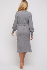 woman wearing a long grey maternity sweater dress with a belted waist, showing a subtle slit at the back