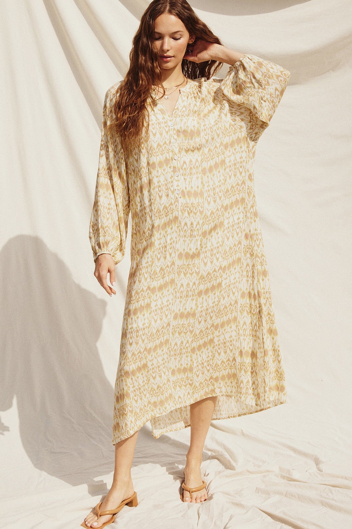 woman wearing a yellow and white patterned midi dress with long sleeves and a v-neckline