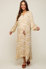 woman wearing a patterned cream and gold maternity maxi dress with long sleeves and a tassel detail