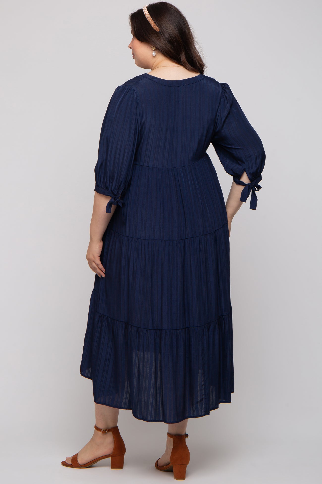 woman wearing a navy blue maternity plus-size tiered maxi dress with puff sleeves and adjustable bows at the cuffs