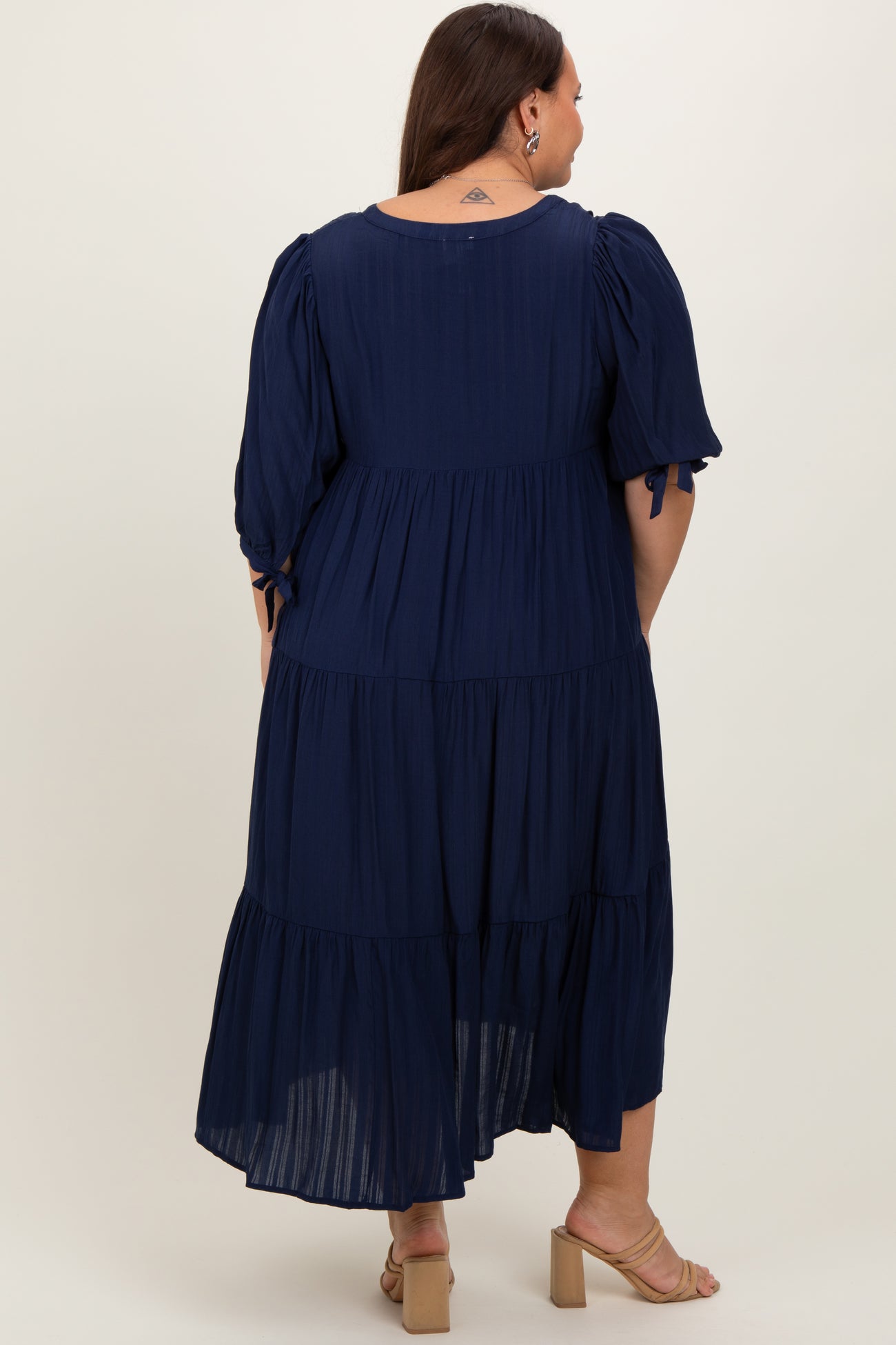 woman wearing a navy blue plus size maxi dress with puff sleeves and tiered ruffle detailing from the back