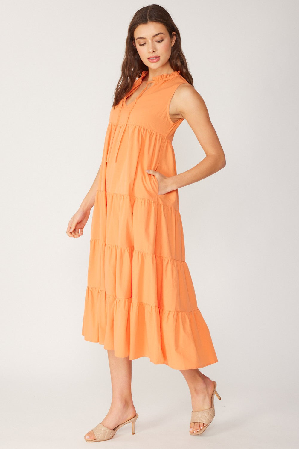 woman wearing an orange tiered midi dress with a collared neckline and pockets, standing sideways