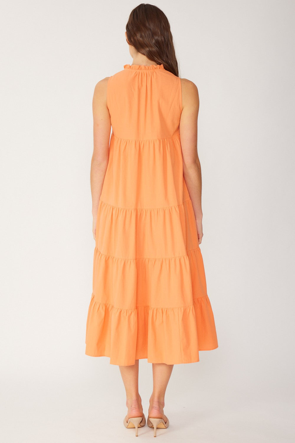 woman wearing an orange tiered midi dress with a ruffled neckline, shown from the back