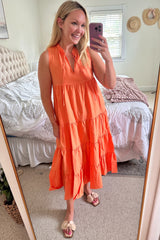 woman wearing an orange tiered maxi dress with a halter neck and pockets, standing in front of a mirror
