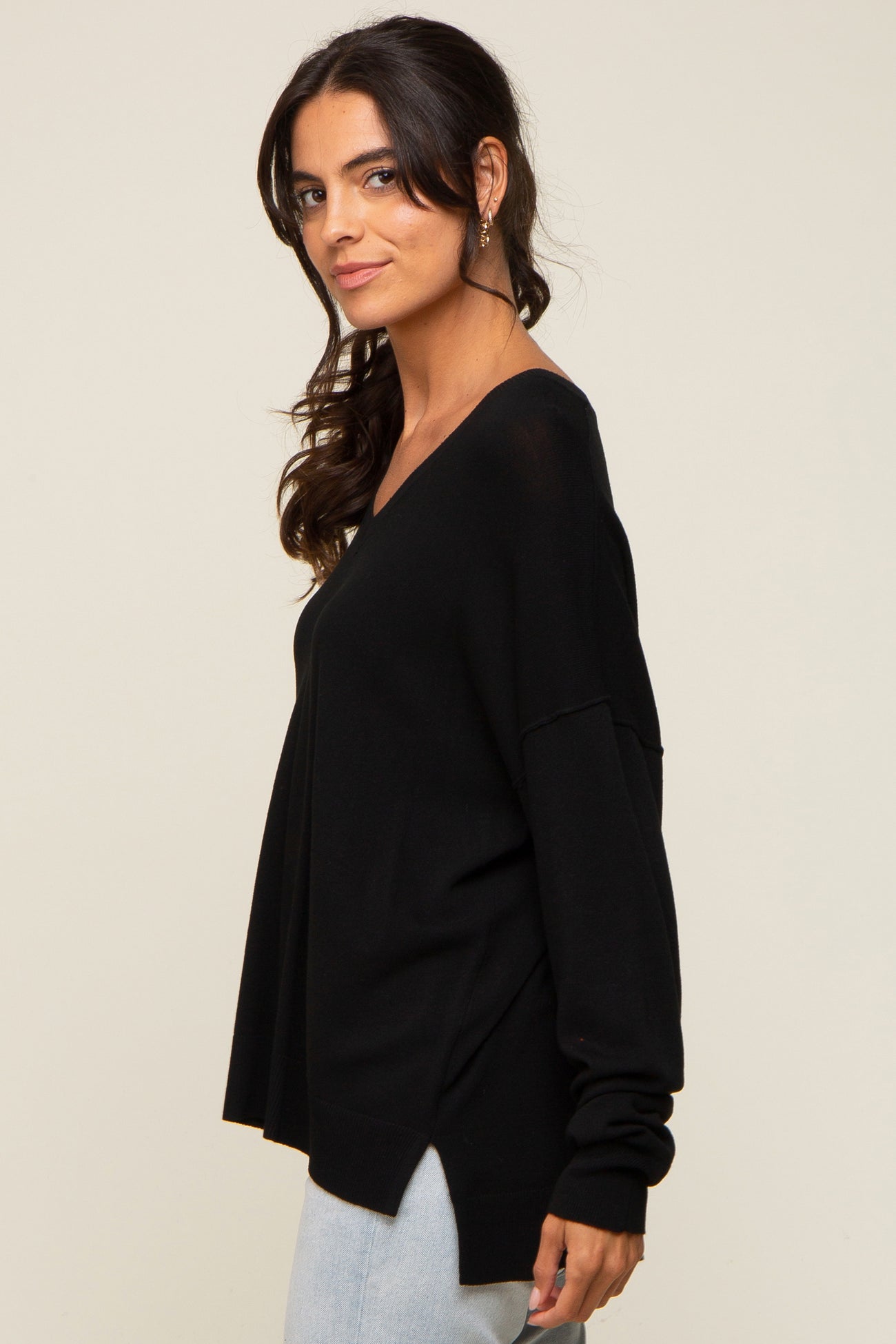 Woman wearing a black long sleeve v-neck sweater with side slits and light wash jeans