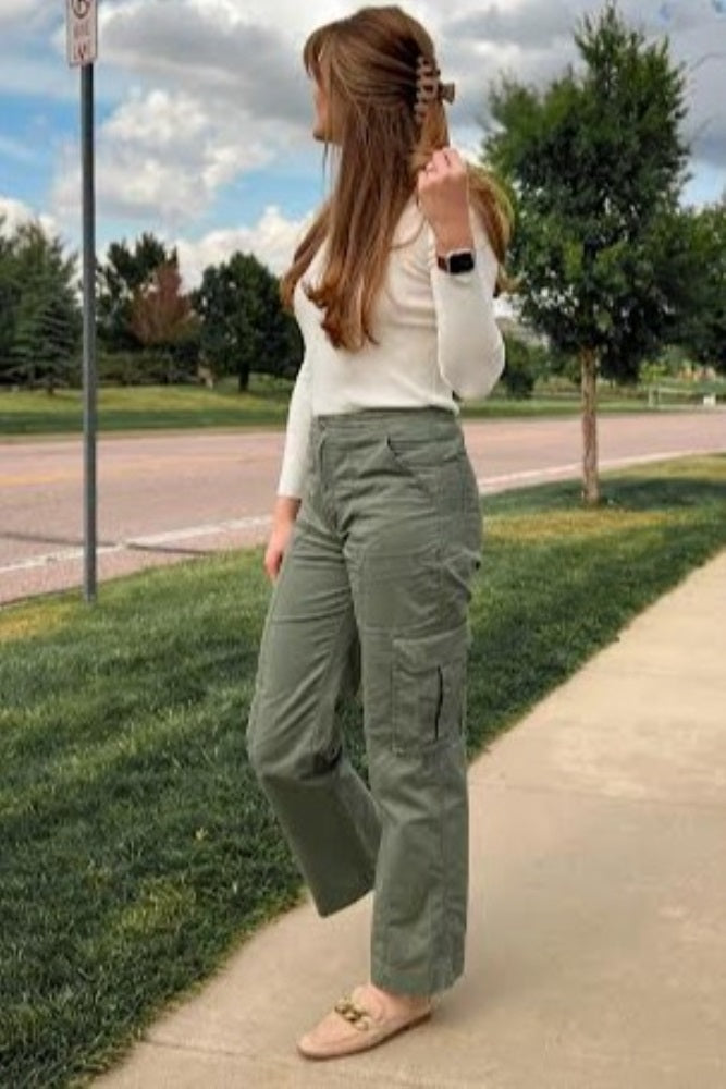 woman wearing olive green cargo pants and white long sleeve shirt standing on a sidewalk