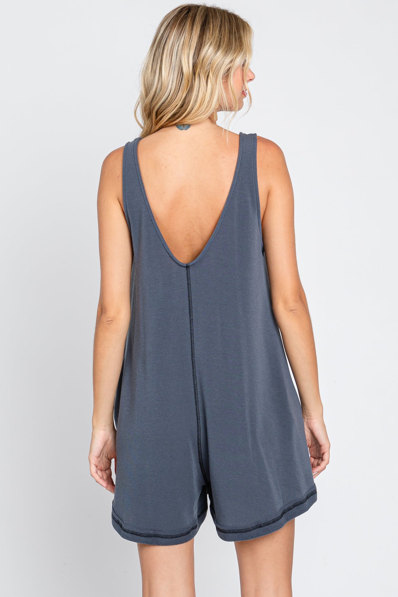 Back view of a woman wearing a charcoal grey sleeveless romper with a deep V-neck back and center seam detail