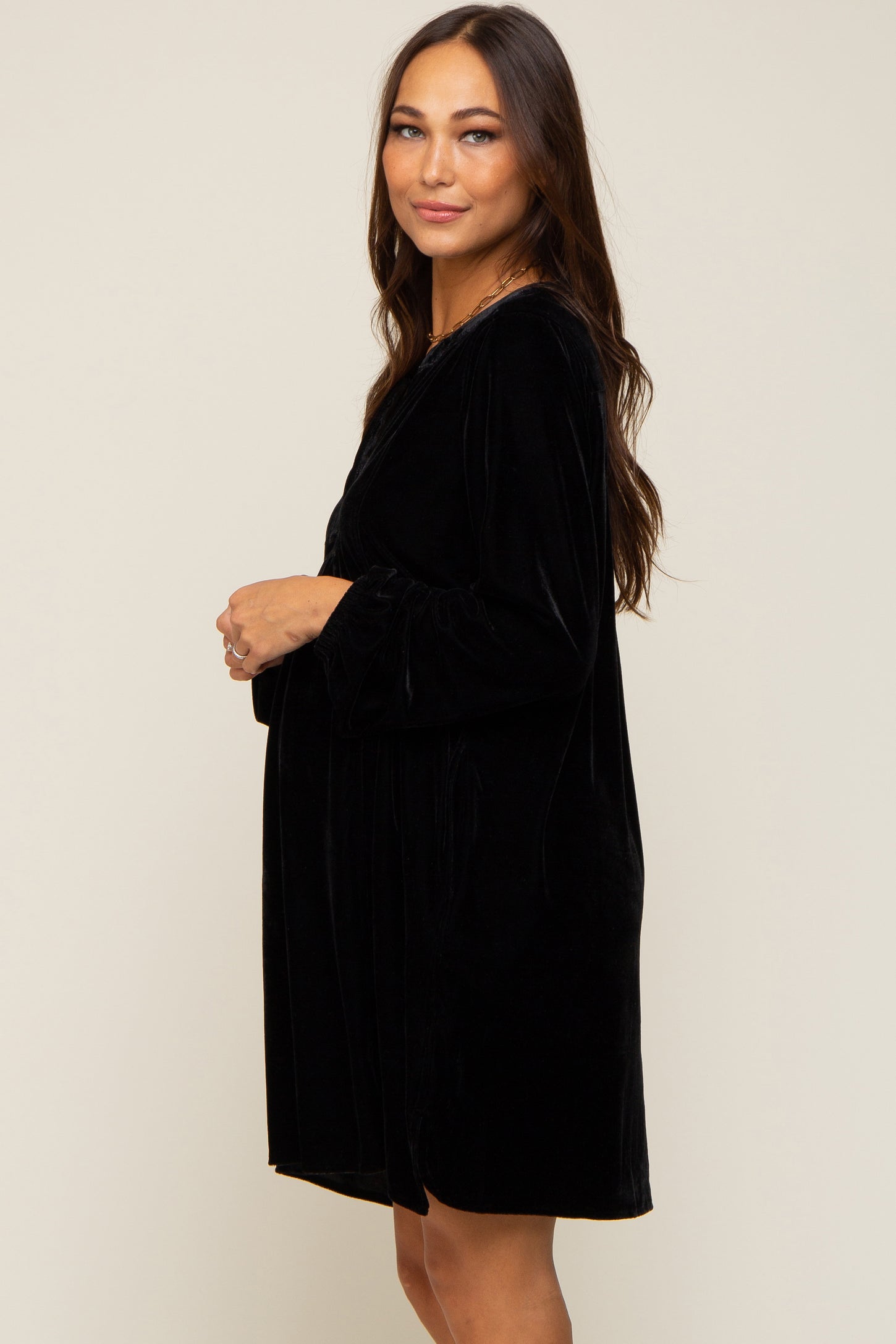 Pregnant woman wearing a long-sleeved black velvet maternity dress against a neutral background