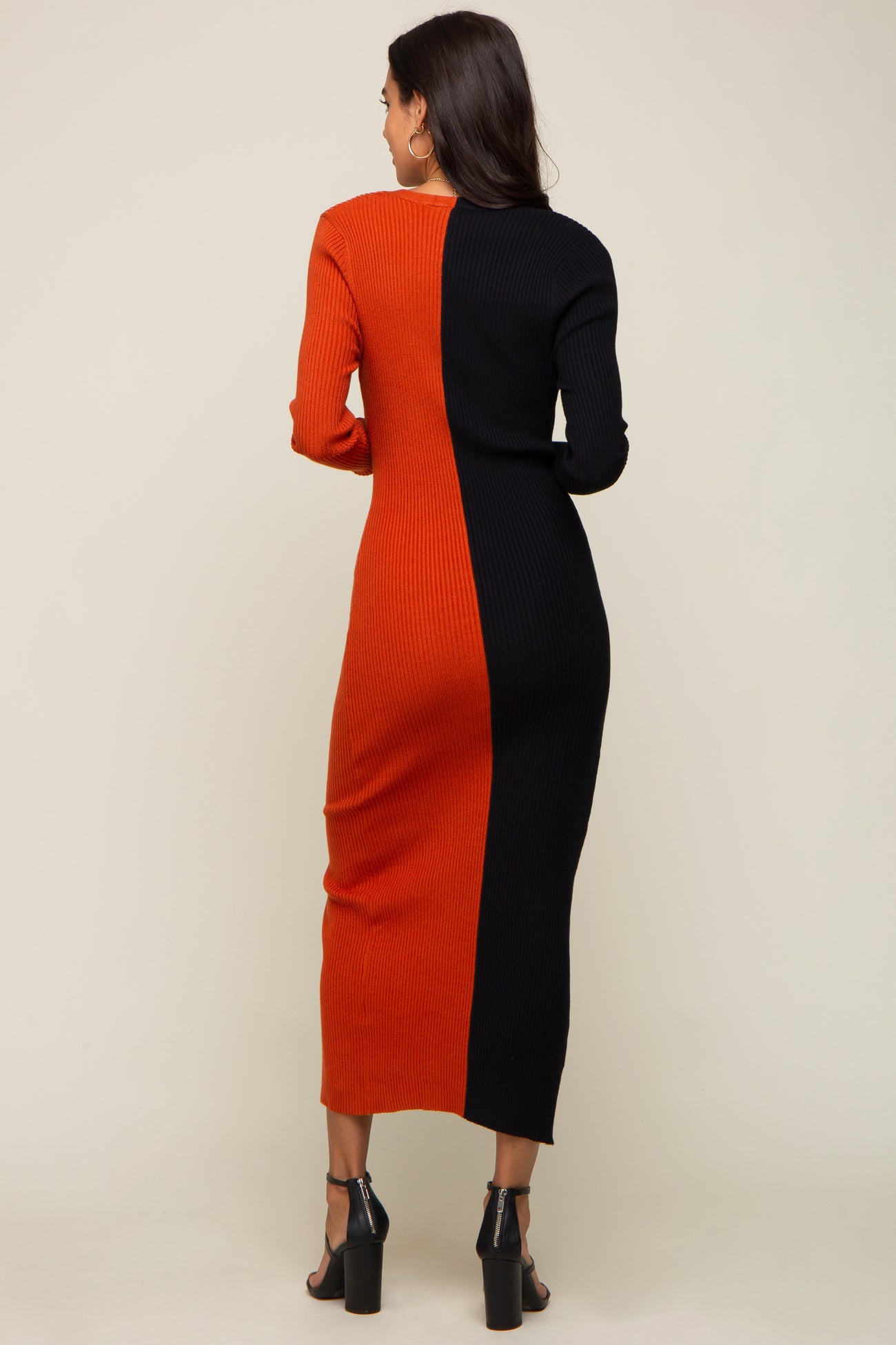 Woman from behind wearing a two-tone orange and black ribbed knit midi dress with long sleeves and black heels