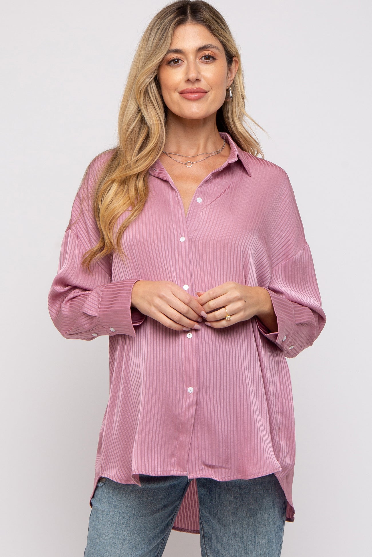 woman wearing a light pink maternity blouse with a ribbed texture and button-down front, paired with denim jeans