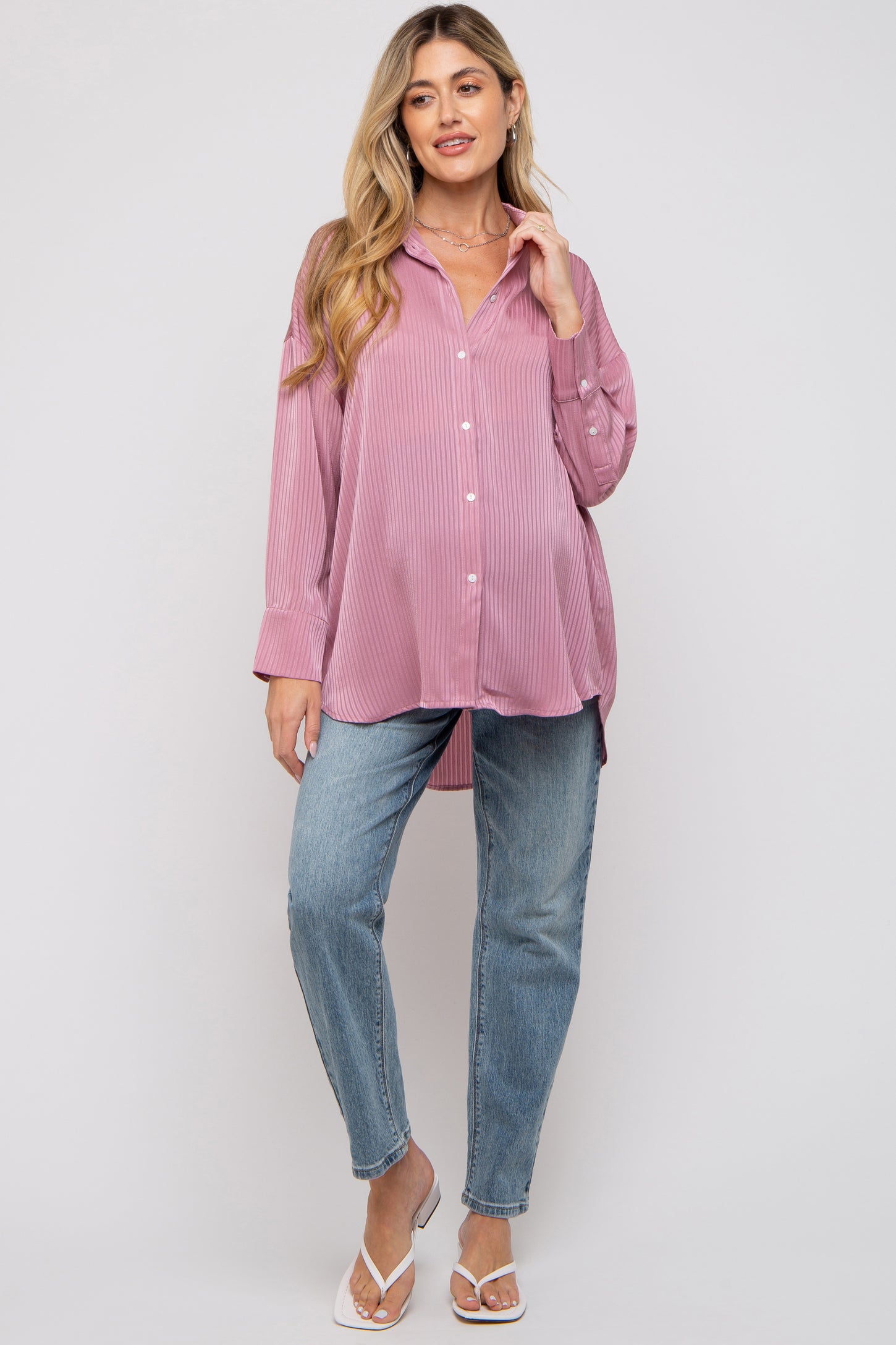 woman wearing a light pink striped oversized maternity shirt and blue jeans, showing her baby bump