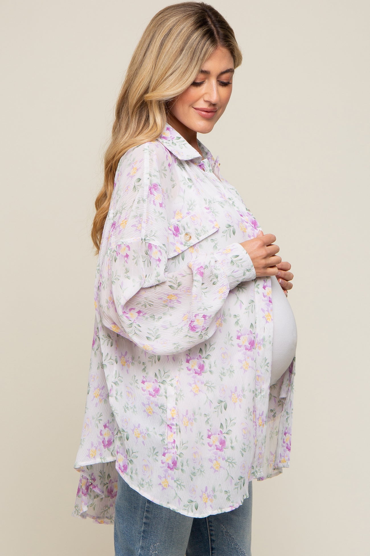 Pregnant woman wearing a floral maternity button-down shirt and jeans holding her baby bump