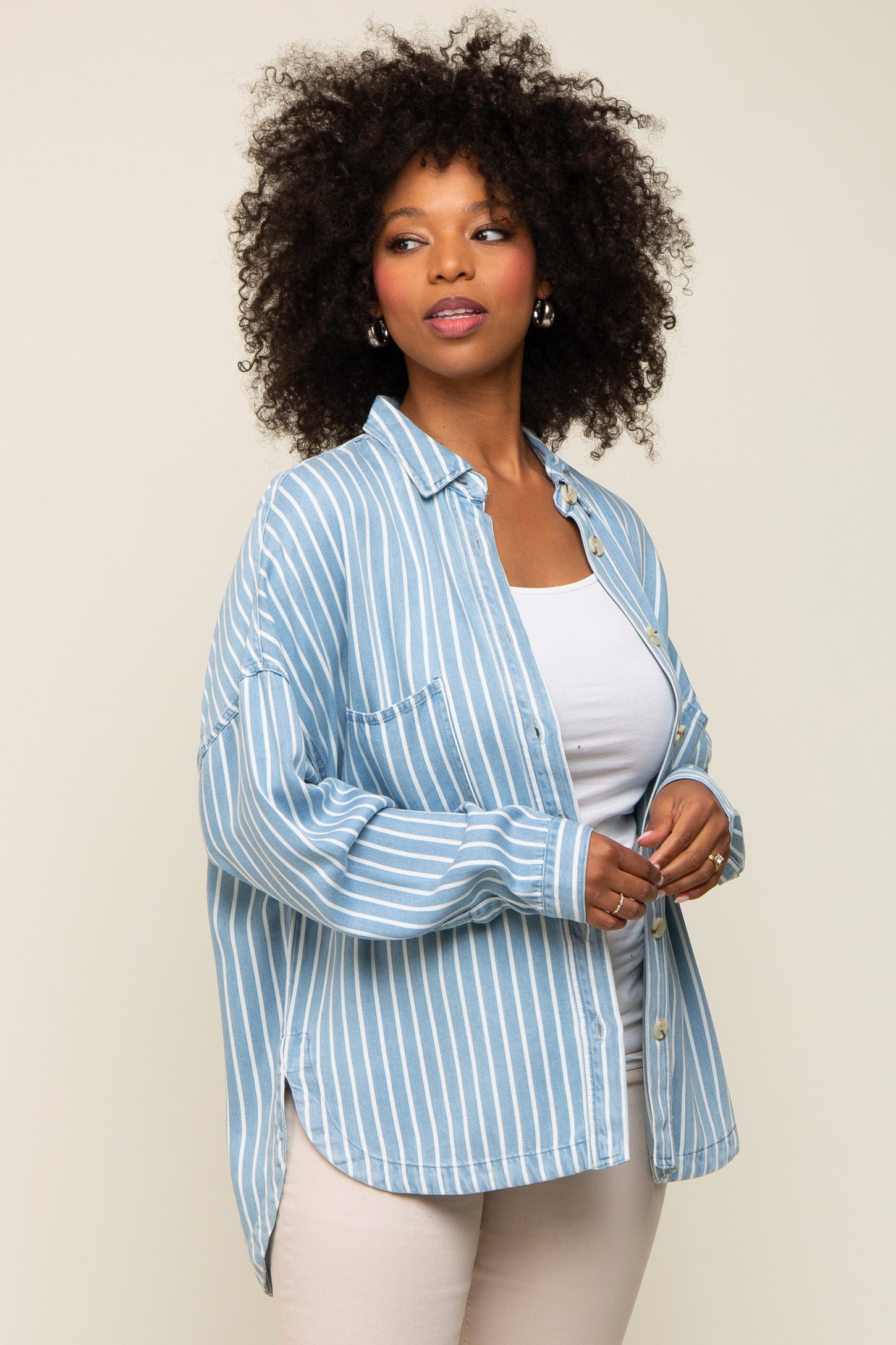 Woman with curly hair wearing a blue and white striped button-down shirt over a white top and beige pants