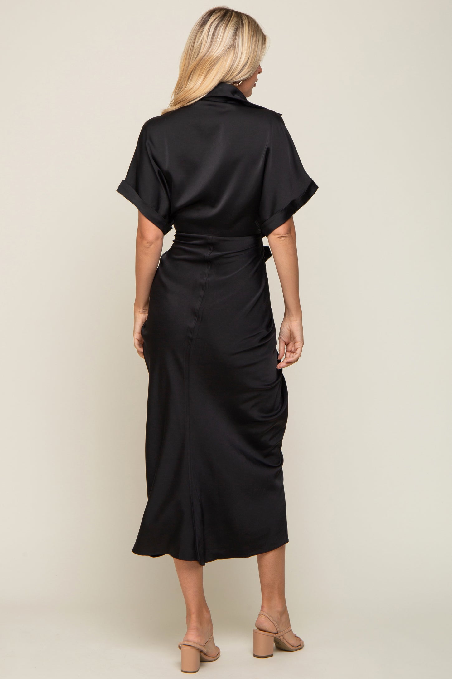 Back view of a woman wearing a black satin midi dress with short sleeves and a belted waist.