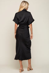 Back view of a woman wearing a black satin midi dress with short sleeves and a belted waist.