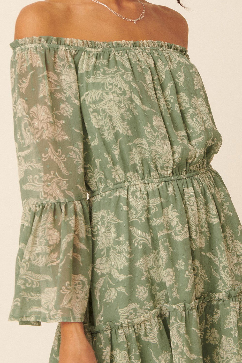 woman wearing a green off-the-shoulder floral print dress with flared sleeves and a tiered skirt