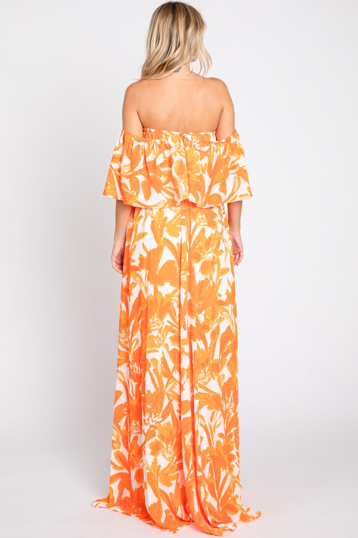woman wearing an orange floral off-the-shoulder maxi dress, showing the back view with flowing fabric and a flared sleeve design