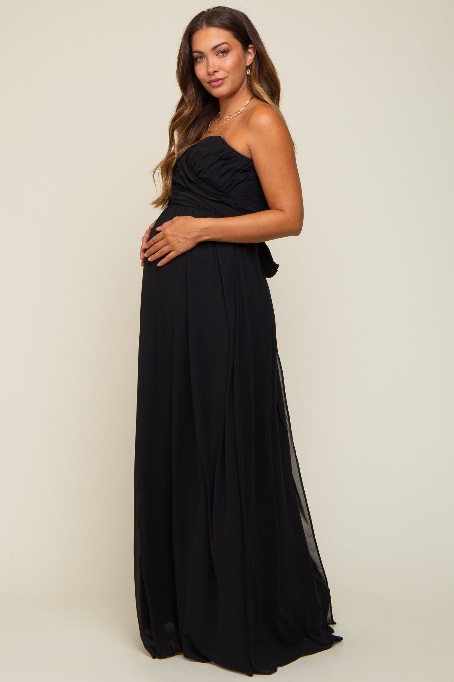woman wearing a black strapless maternity maxi dress, showing her baby bump and posing elegantly