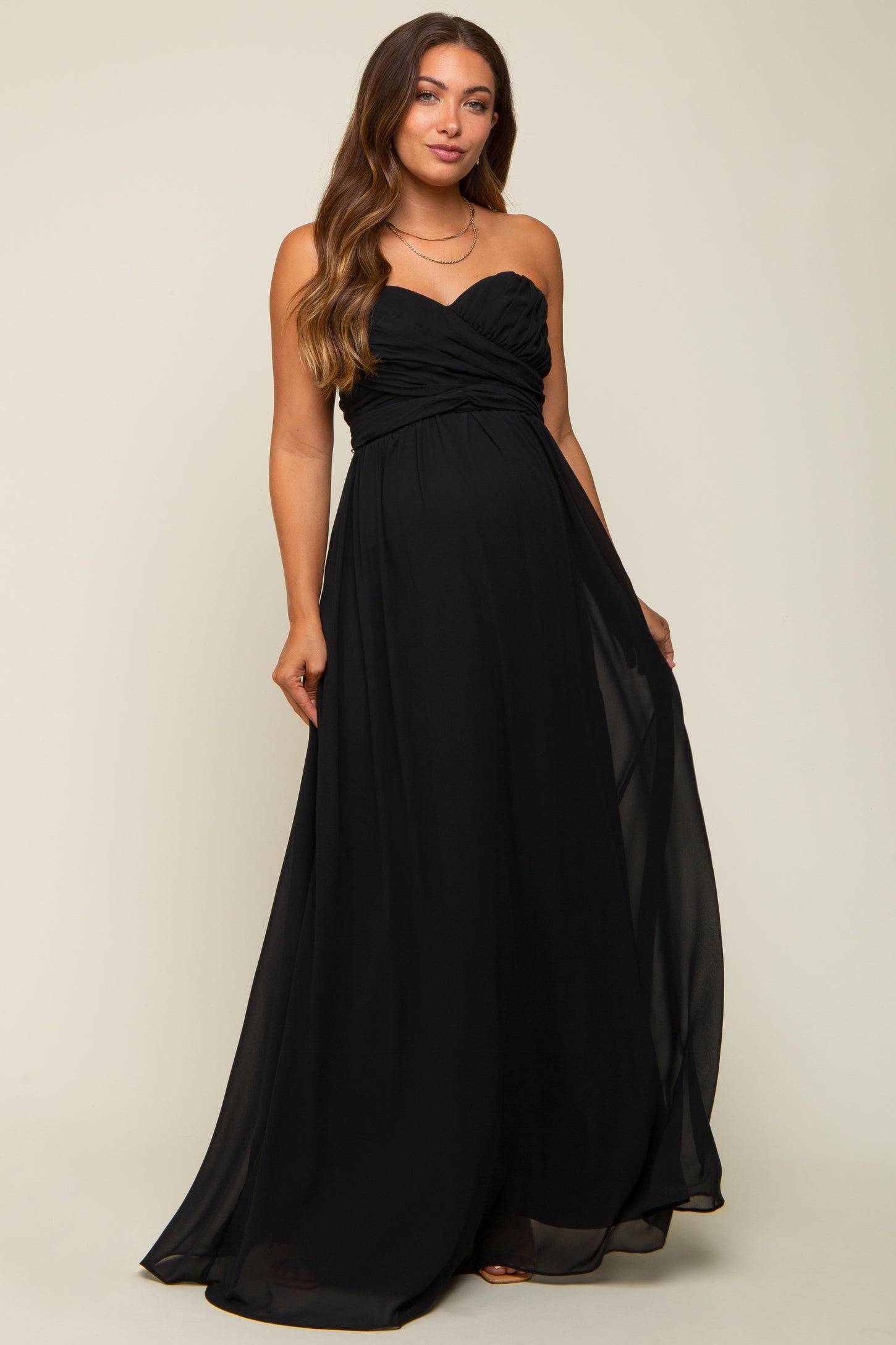 woman wearing a black strapless maternity gown with a ruched bodice and flowing skirt, showcasing her baby bump