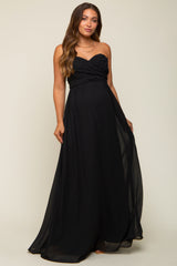 woman wearing a black strapless maternity gown with a ruched bodice and flowing skirt, showcasing her baby bump