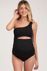woman wearing a black one-shoulder maternity swimsuit with a cutout detail and gathered sides, highlighting her baby bump