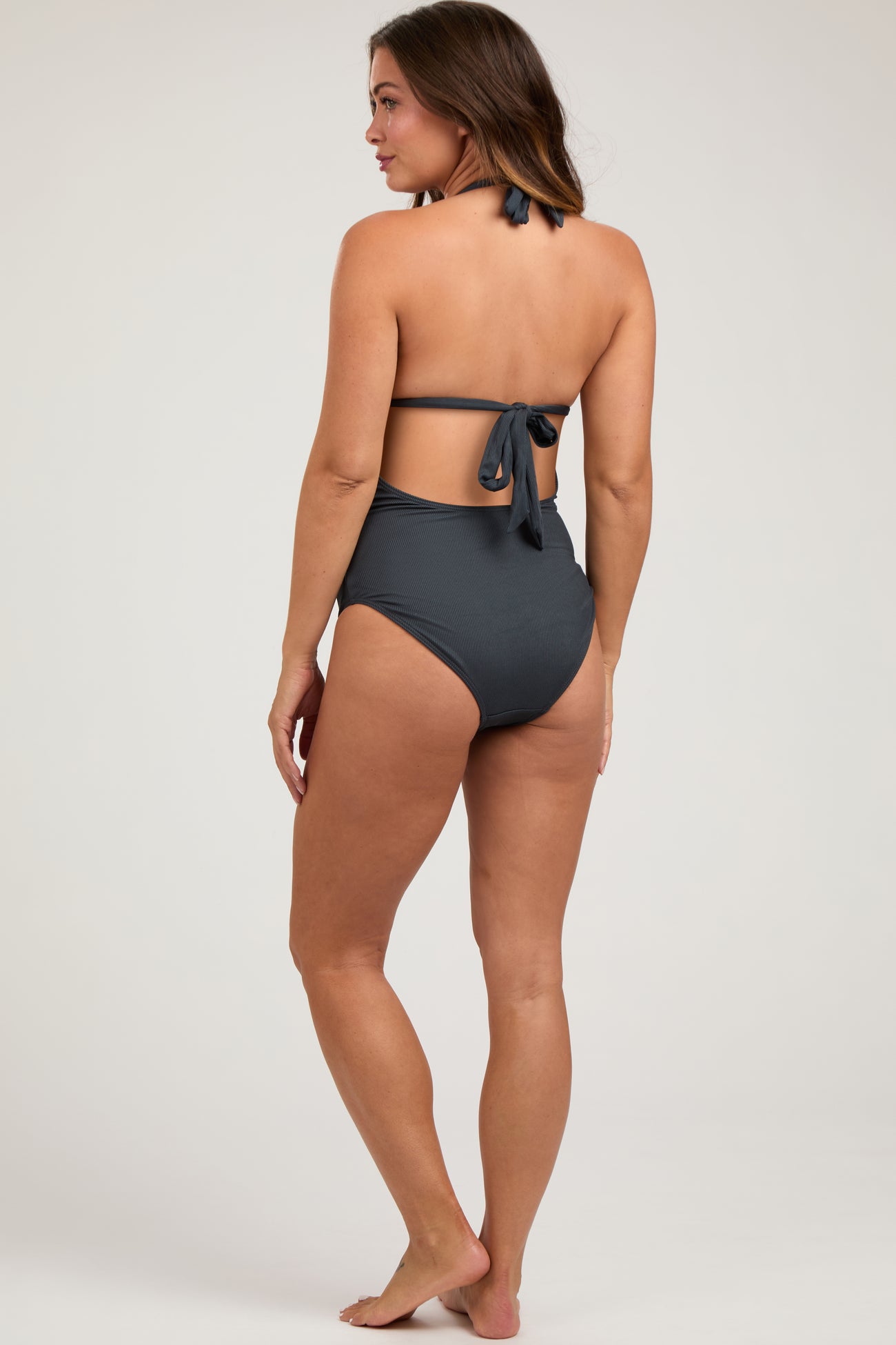 woman wearing a dark gray maternity swimsuit with a tie-back detail and high waist from the back
