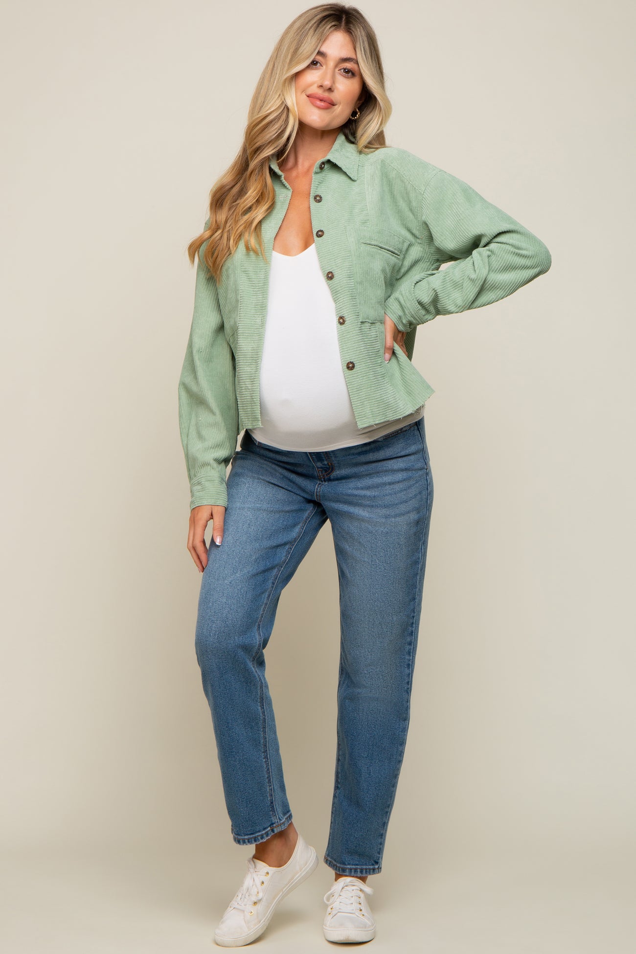 Pregnant woman wearing a sage green corduroy shirt, white maternity top, and blue jeans