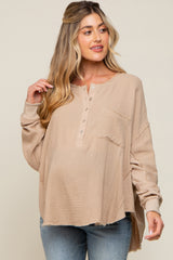 woman wearing a beige maternity top with a front pocket and button details, showcasing her baby bump