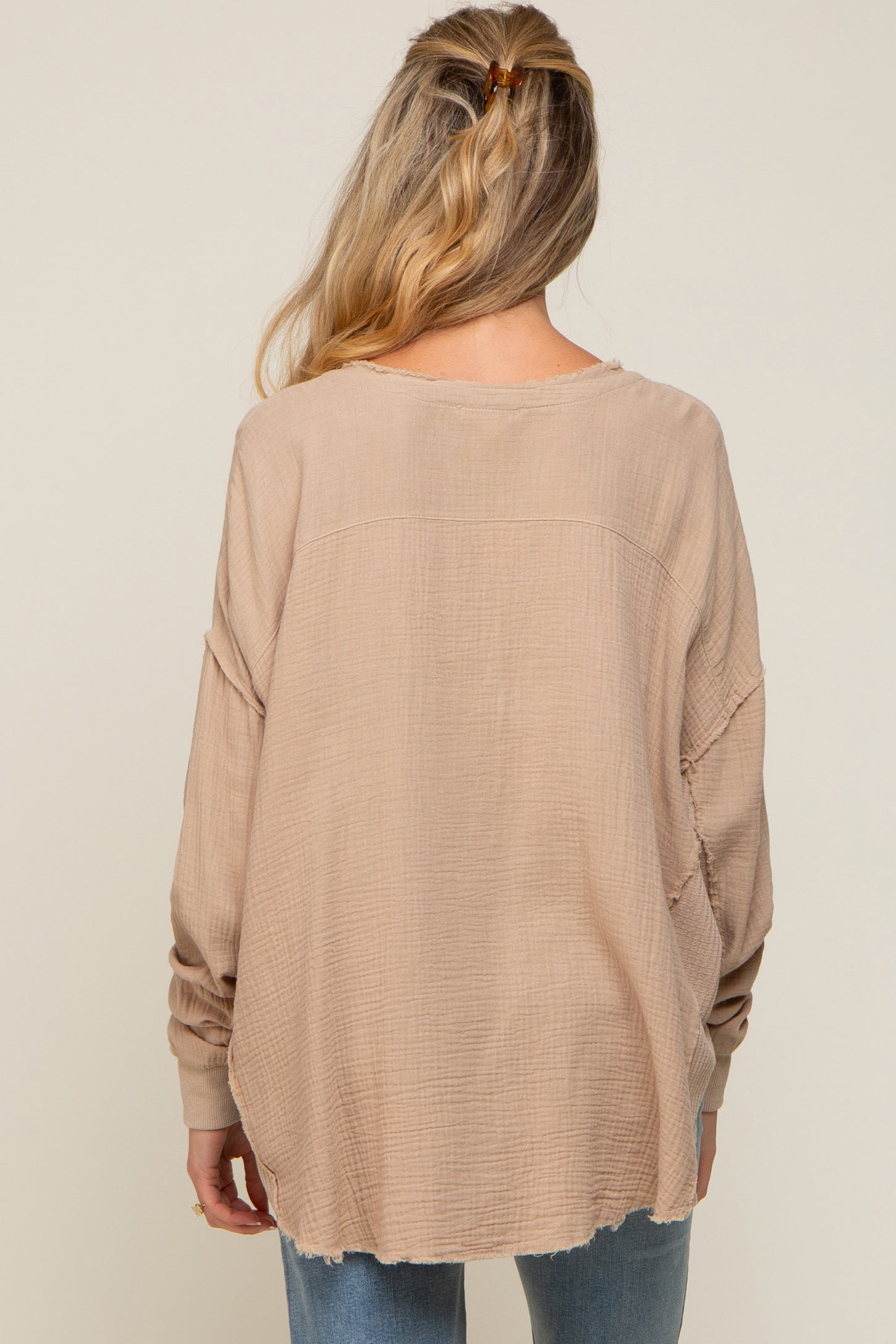 woman wearing a loose beige maternity top with long sleeves and a relaxed fit, seen from the back