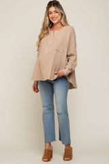 woman wearing a beige maternity top with buttons and long sleeves, paired with light blue distressed jeans and a baby bump visible