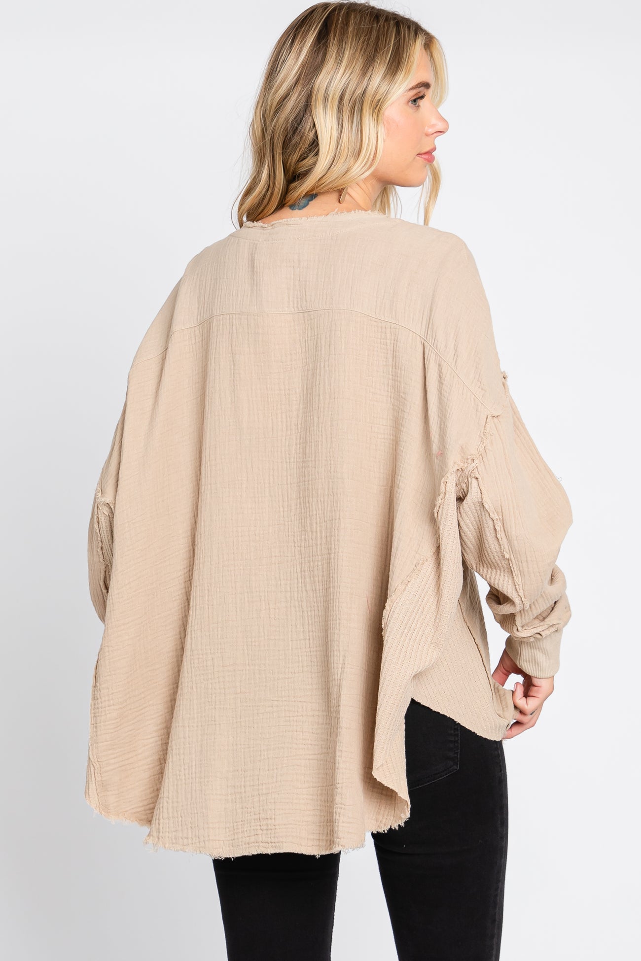 woman wearing a beige oversized long sleeve top with a relaxed fit and textured fabric, seen from the back