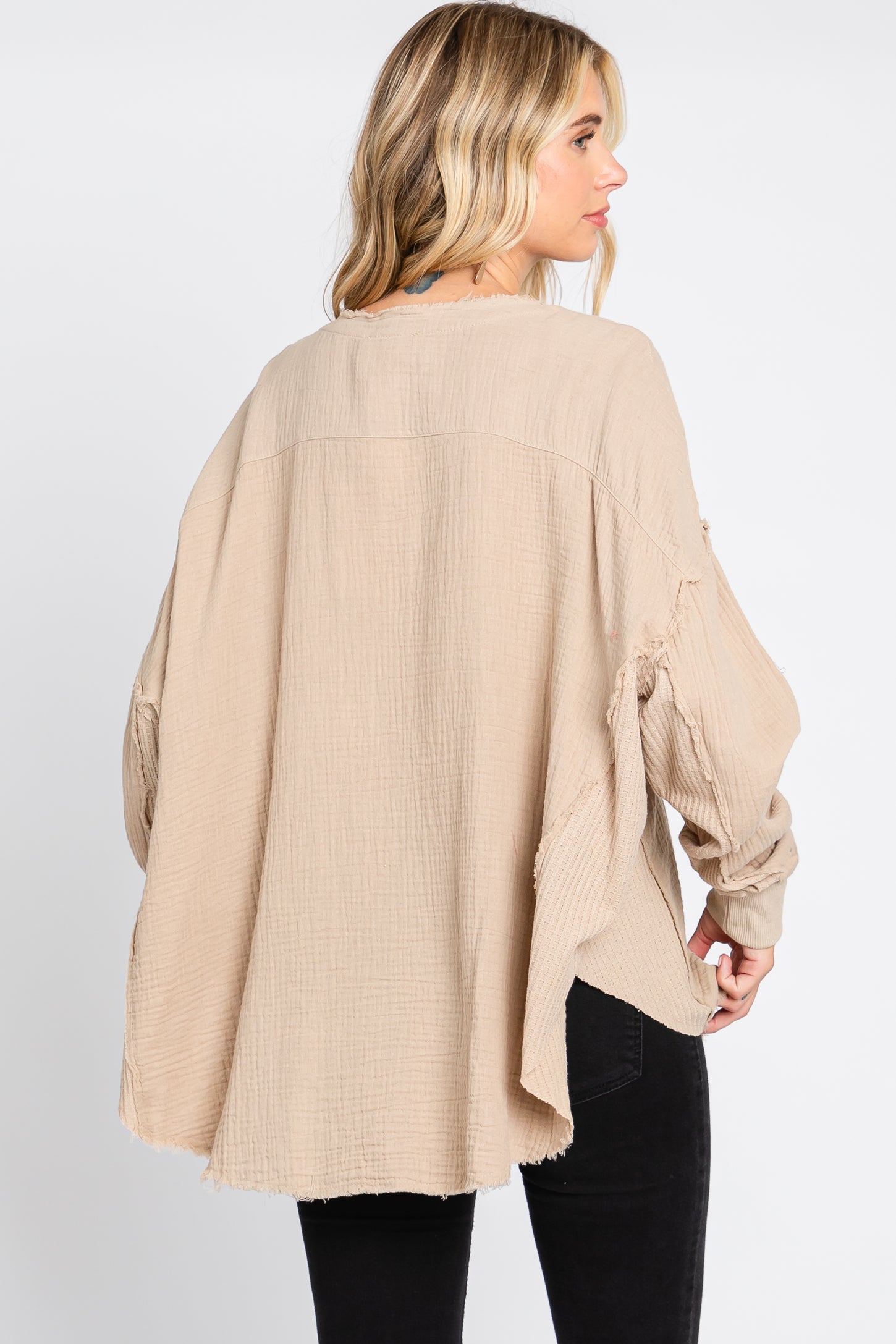 woman wearing a beige oversized long sleeve top with a relaxed fit and textured fabric, seen from the back