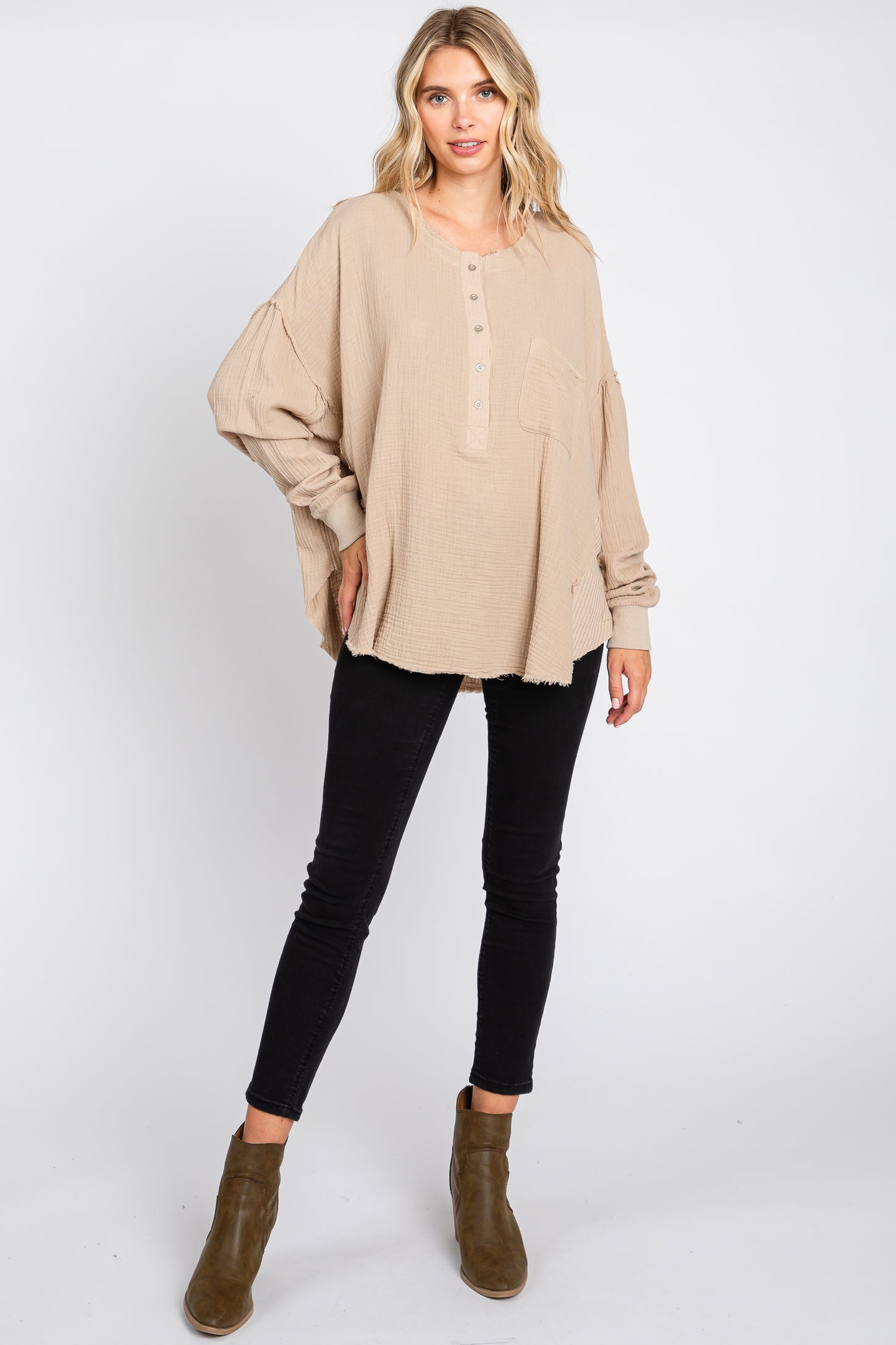 woman wearing a light beige oversized henley top with button details and a pocket, paired with black skinny jeans and ankle boots