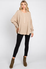 woman wearing a light beige oversized henley top with button details and a pocket, paired with black skinny jeans and ankle boots