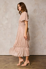 woman wearing a blush pink shimmer wrap dress with flutter sleeves and ruffled hem