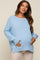 woman wearing a light blue oversized maternity sweater and gently cradling her baby bump
