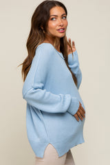 woman wearing a light blue oversized maternity sweater, showing off her baby bump with one hand on her belly