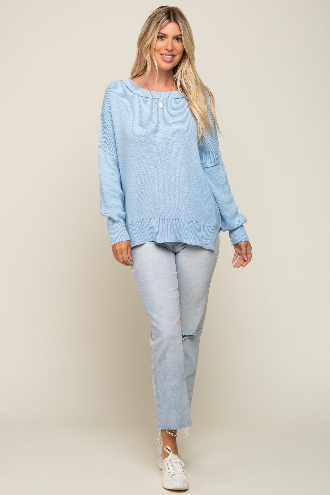 woman wearing a light blue oversized sweater with a round neckline and light blue distressed jeans