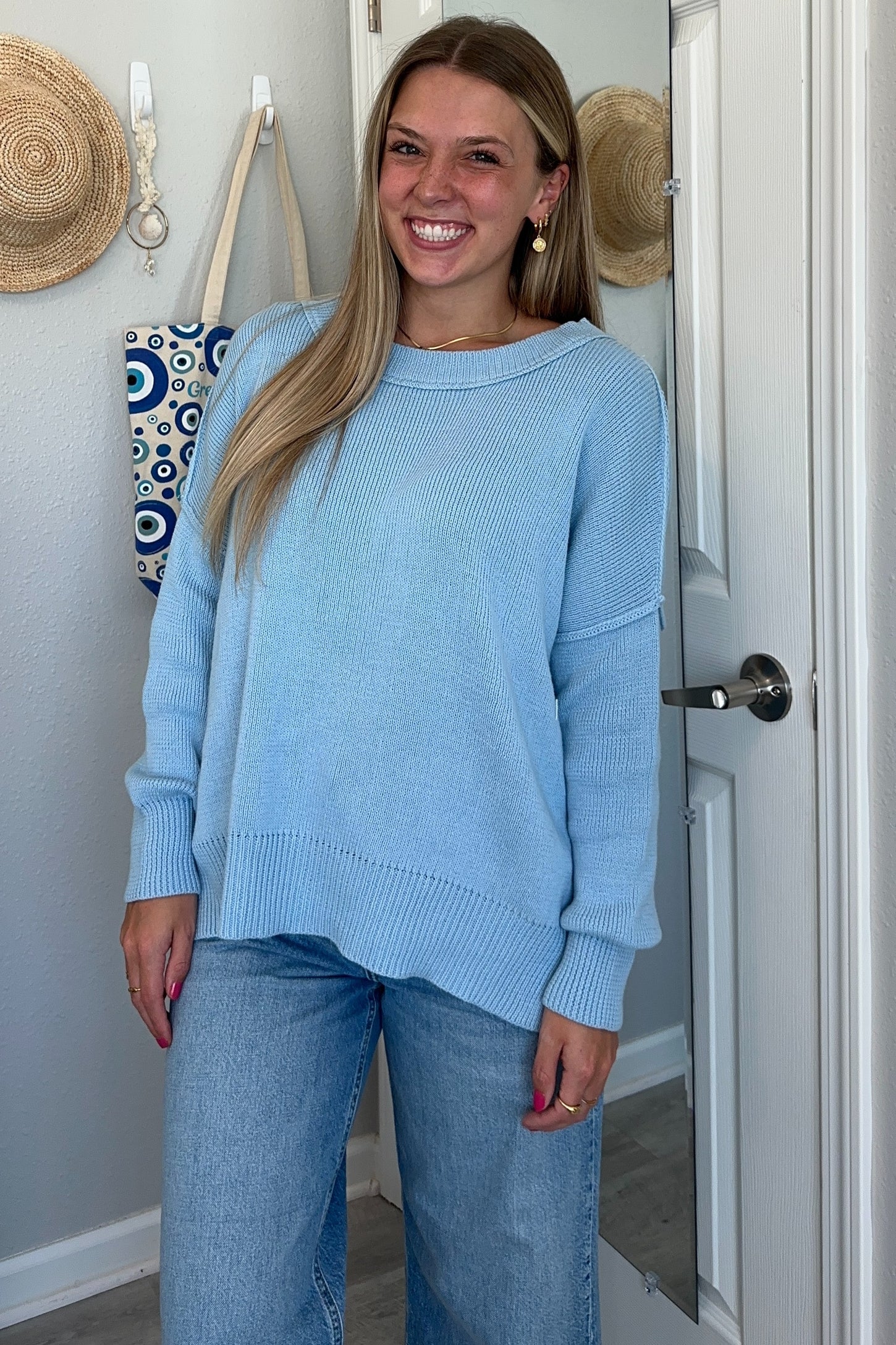 woman wearing a light blue oversized knit sweater and high-waisted jeans, smiling in front of a mirror