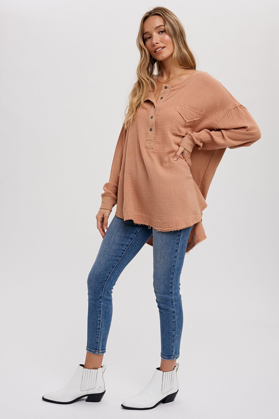 woman wearing oversized terracotta gauze henley top with blue skinny jeans and white ankle boots