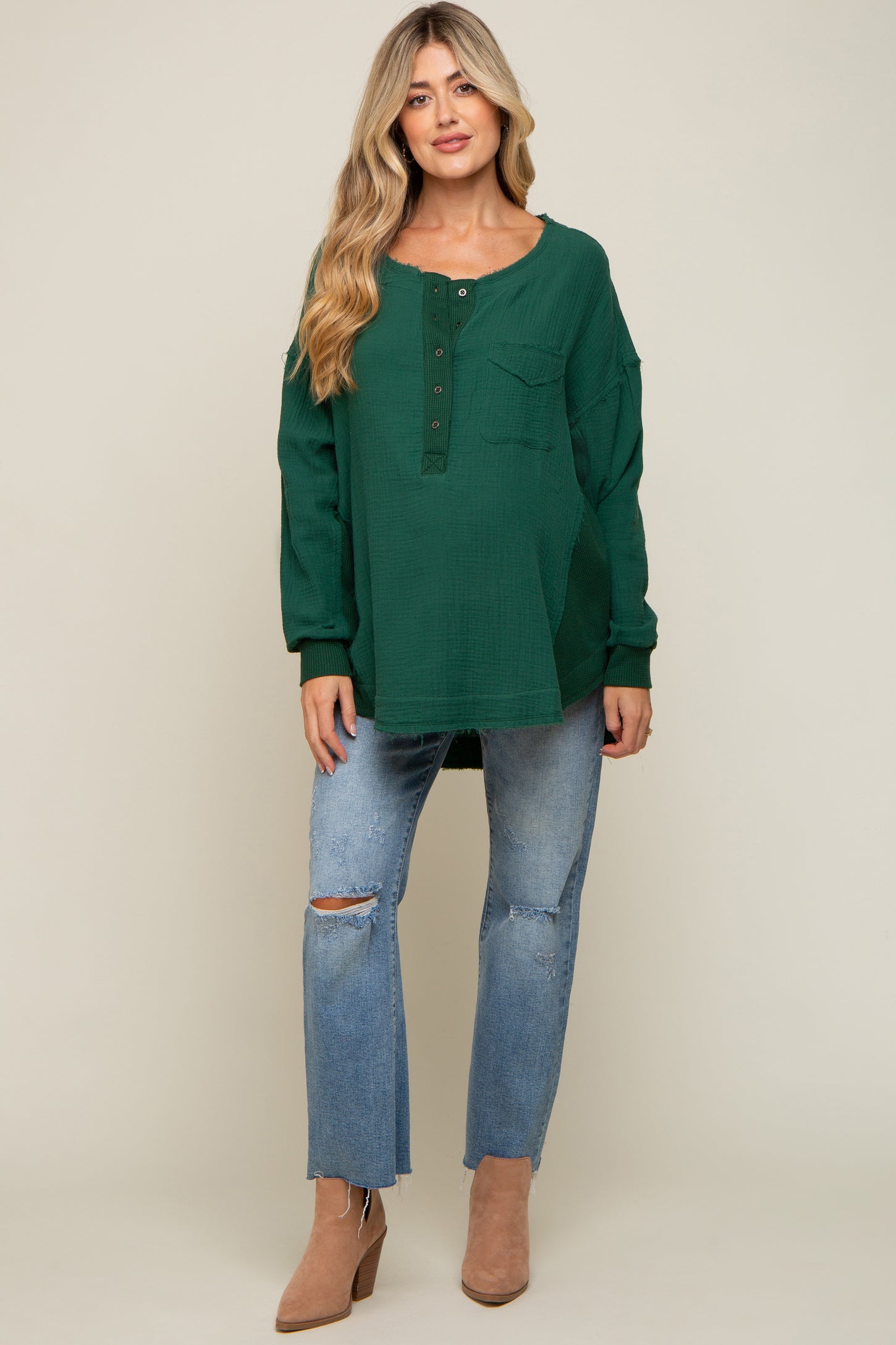 woman wearing a green long sleeve gauze henley top with distressed blue jeans and tan ankle boots