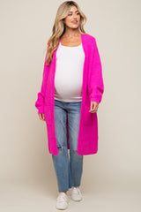 pregnant woman wearing a long hot pink knit maternity cardigan over a white top and distressed blue jeans