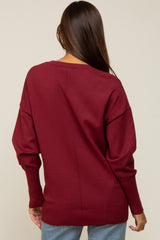 Back view of a woman wearing a burgundy long sleeve knit sweater with seam detail and ribbed cuffs