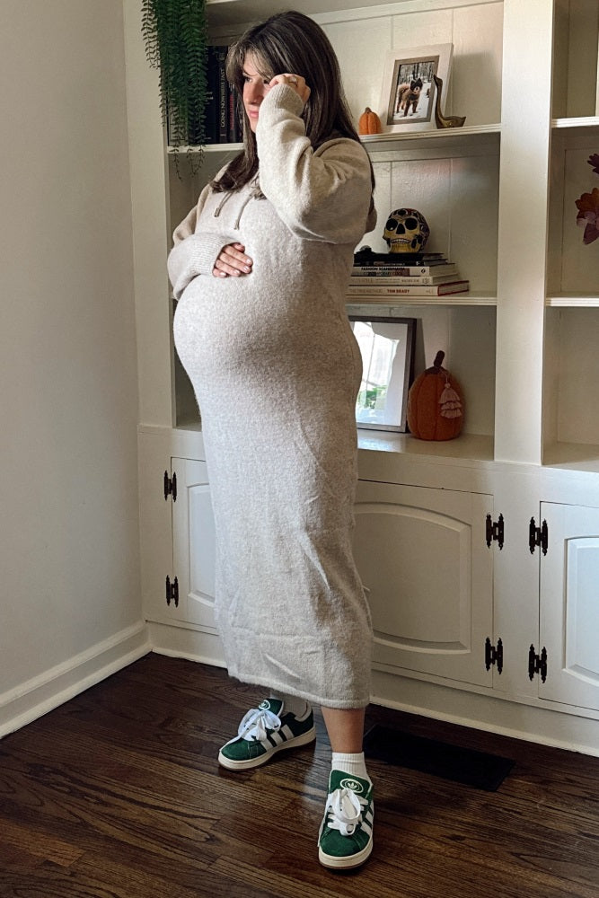 woman wearing a beige long sleeve maternity dress with a visible baby bump and green sneakers