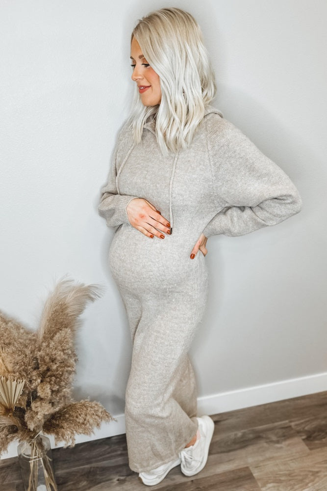 woman wearing a light gray maternity hoodie dress and holding her baby bump