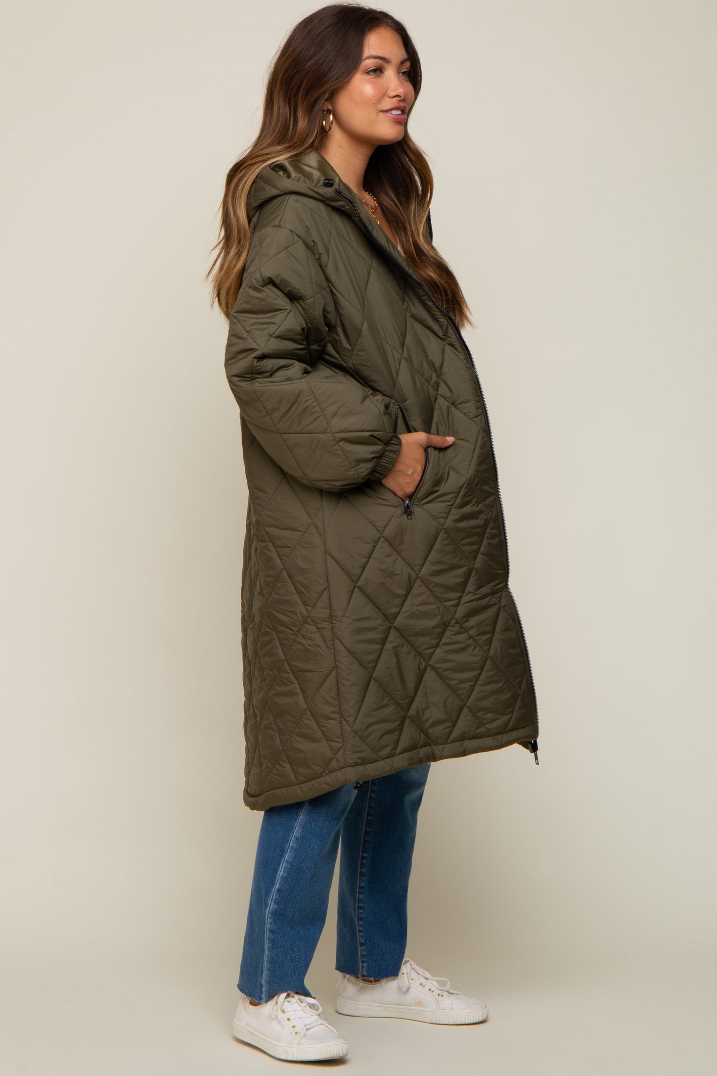 Woman wearing an olive green quilted long puffer coat with a hood and blue jeans