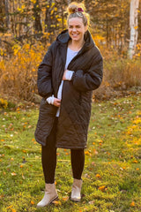 woman wearing a black quilted maternity coat and holding her baby bump in an autumn setting