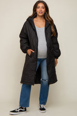 woman wearing a black quilted maternity coat over a gray top and blue jeans, showing her baby bump